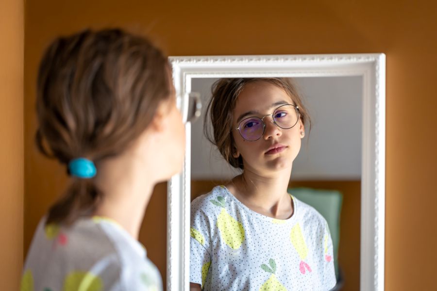 young girl looks unhappily into mirror